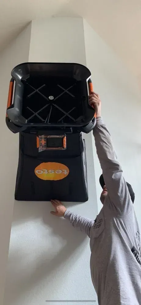A man is holding a black box on top of a white wall.