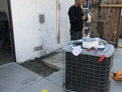 A man is working on an air conditioner outside of a house.