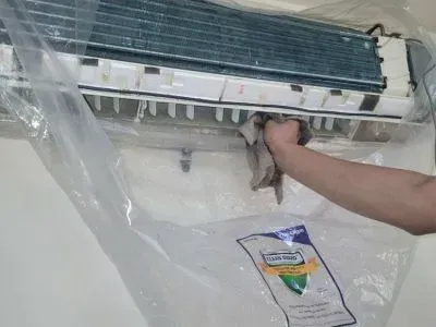 A person is cleaning an air conditioner with a plastic bag.