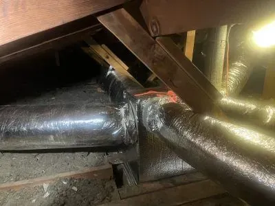 A bunch of pipes are connected to each other in an attic.
