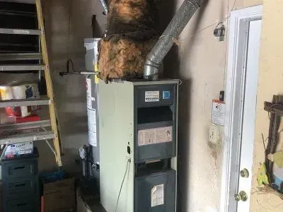 A furnace is sitting in a garage next to a ladder.