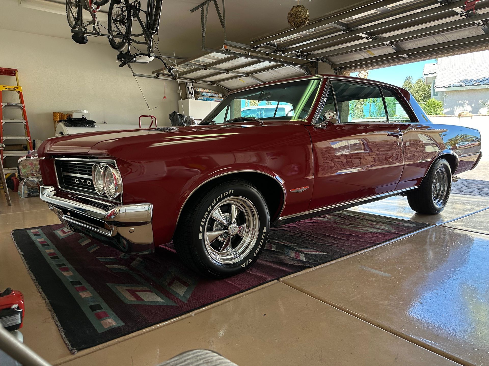 A red car is parked in a garage next to a rug.