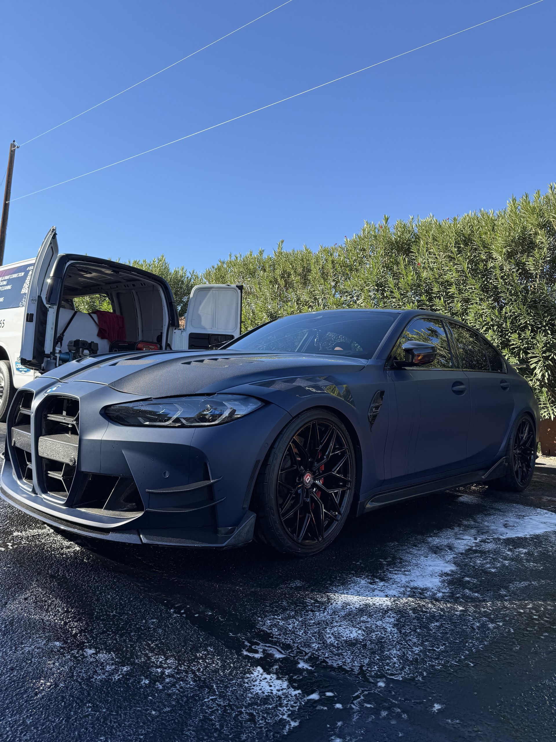 A bmw m4 is parked on the side of the road next to a van.