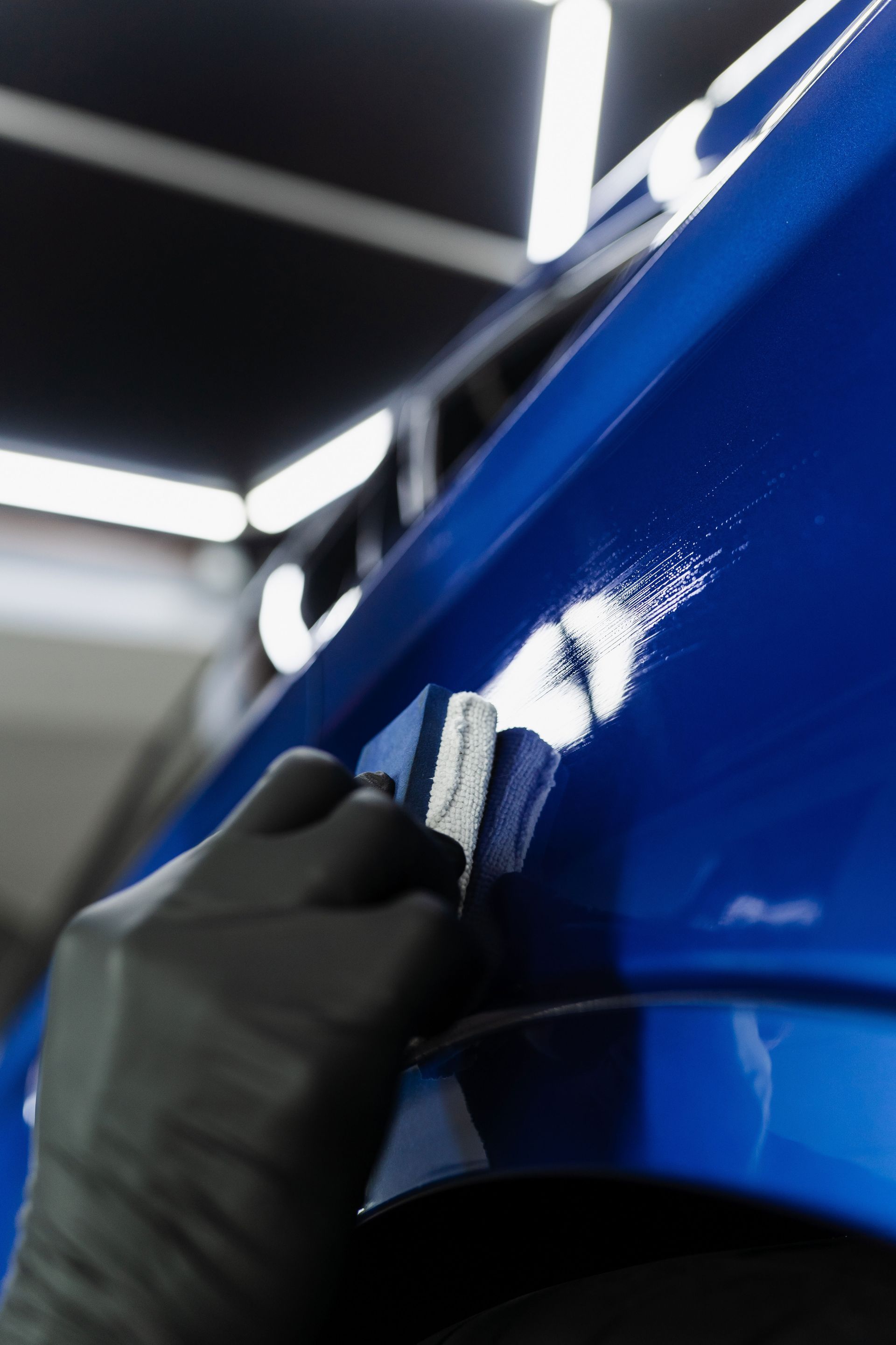 A person is polishing a blue car with a brush.