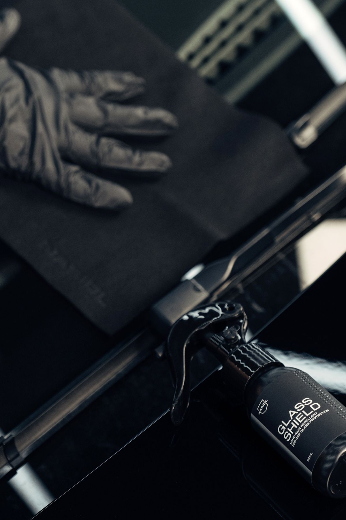 Gloved hand wiping glass with black cloth. Black bottle labeled 