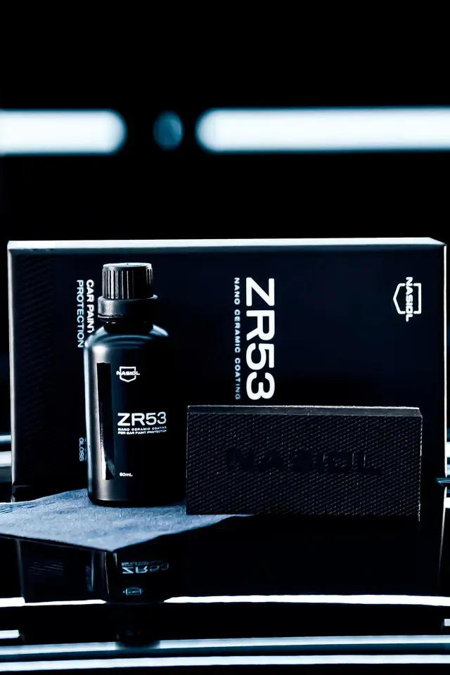 A bottle of ZR53 nano ceramic coating with its box and a carbon fiber application block, set on a dark, reflective surface.