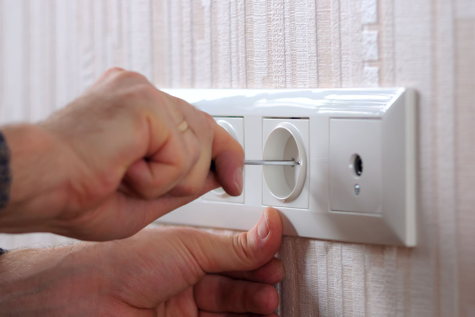 Hands Using A Screwdriver To Work On A White Electrical Outlet — Electrical & Air Cooling Solutions in Townsville, QLD