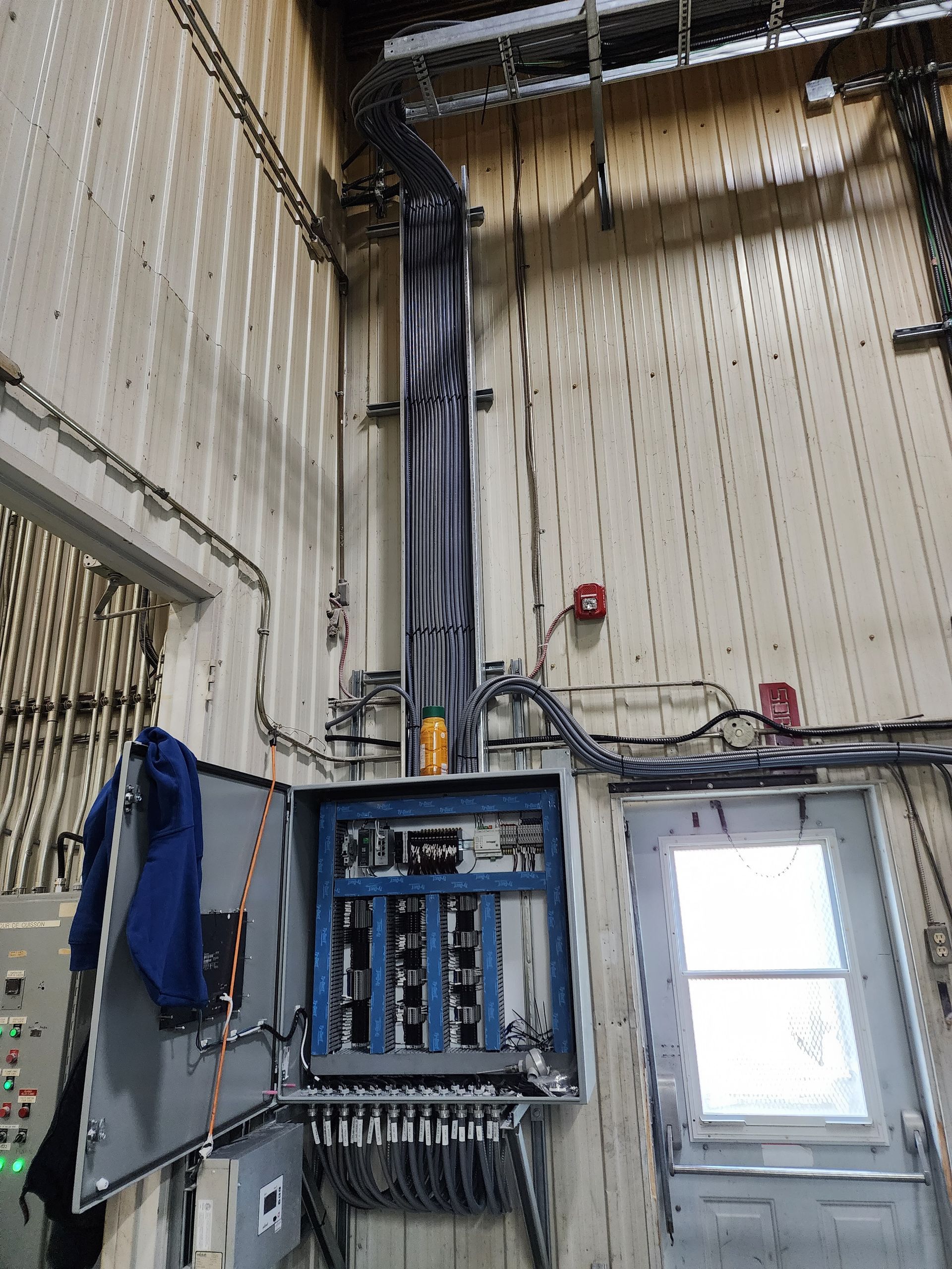 Un tableau électrique industriel avec une porte ouverte et d'épais câbles remontant dans un chemin de câbles métallique fixé au mur.