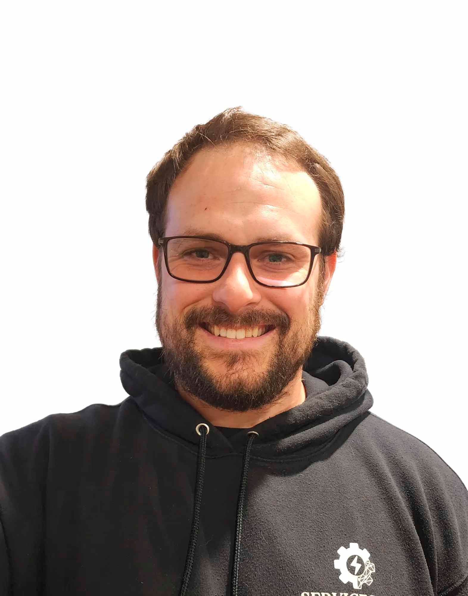 Homme à lunettes et barbe, portant un sweat à capuche noir avec logo, souriant.