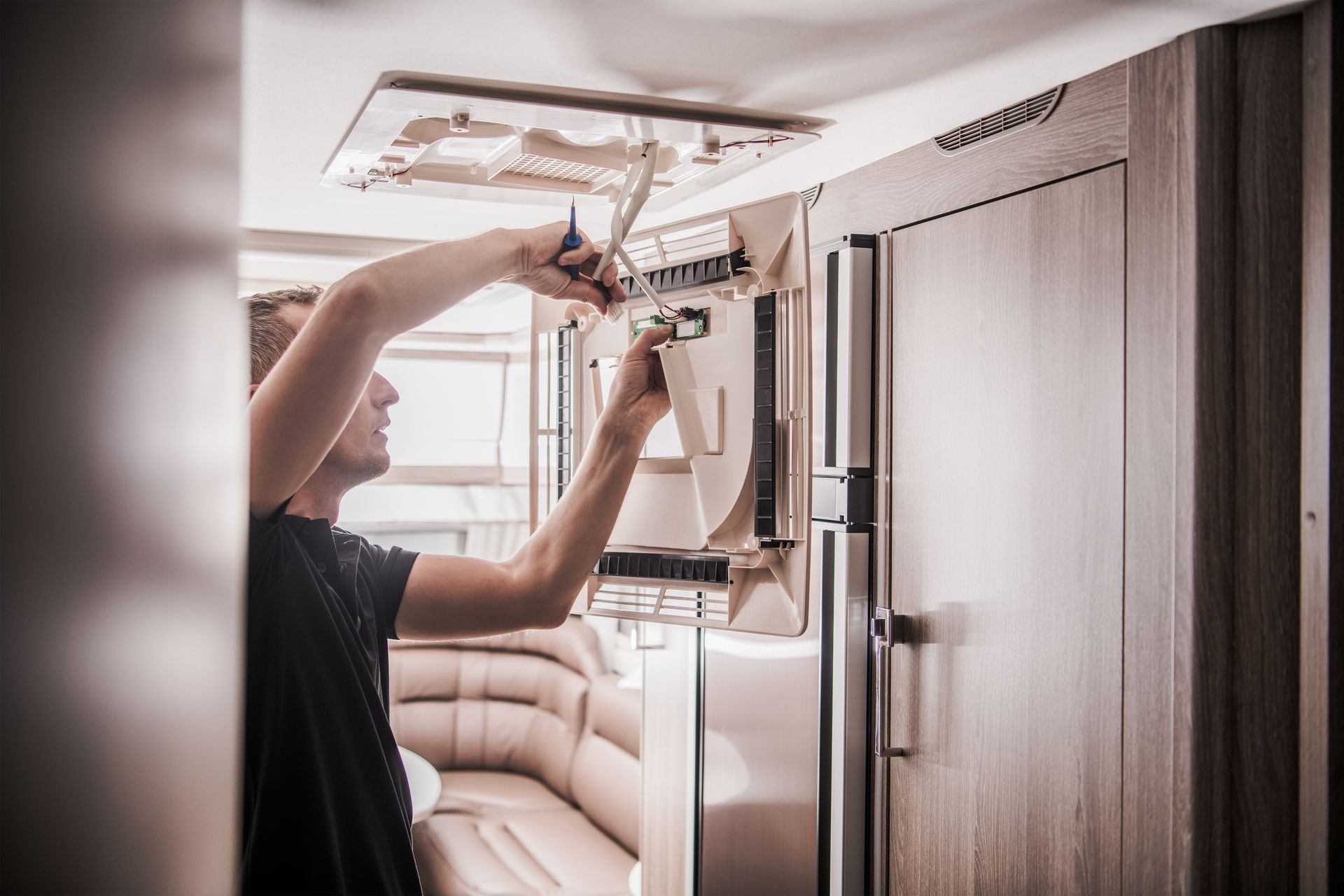 Person hanging clothes in a compact RV closet beside a beige sofa and wood-paneled cabinetry