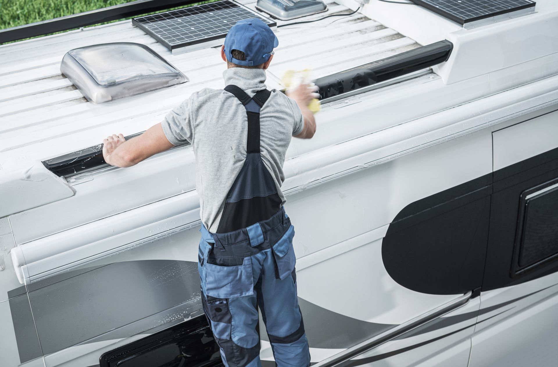 Person cleaning the white roof of a boat, viewed from behind.