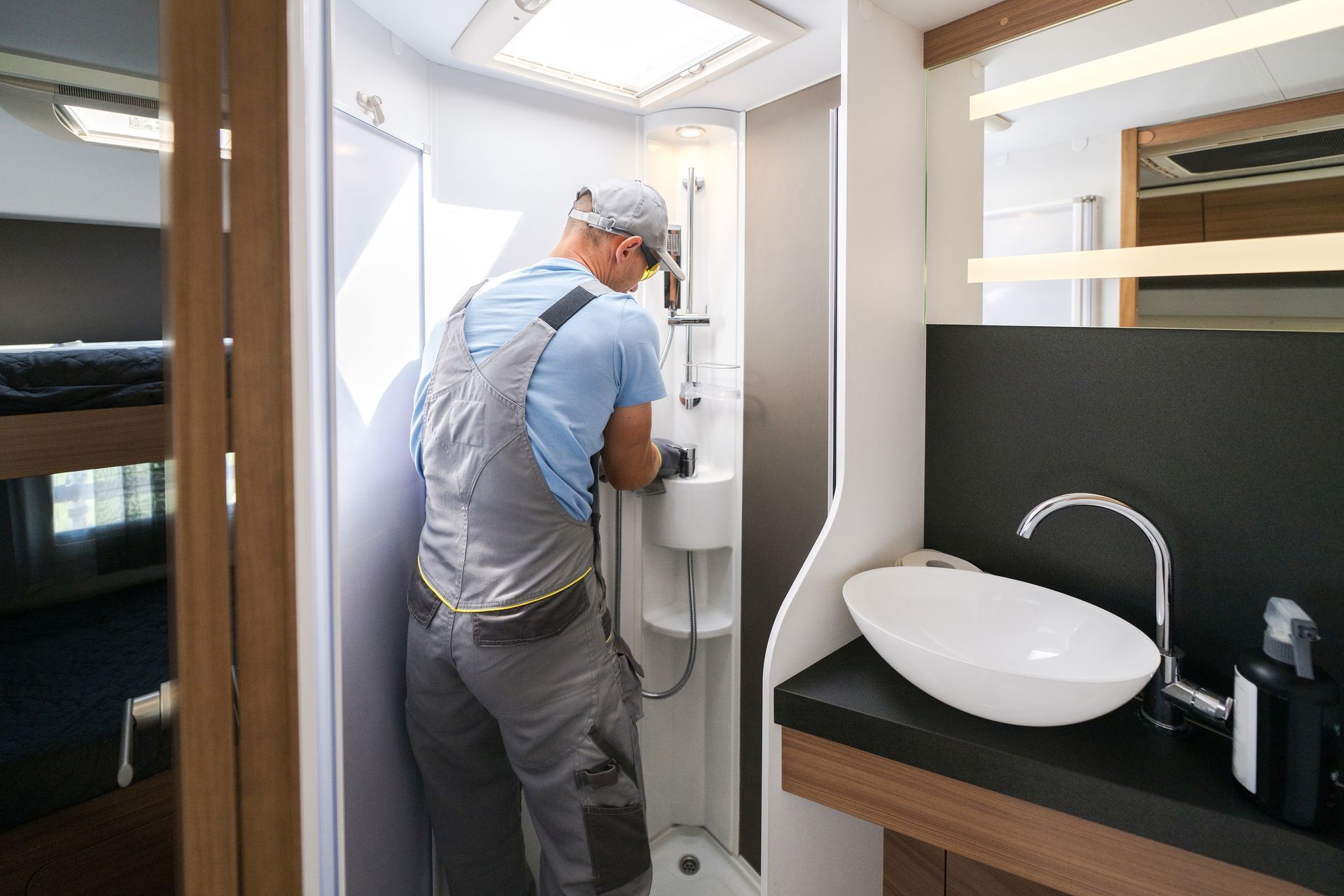 Person using a small restroom sink in a modern bathroom with a round white basin and wood countertop