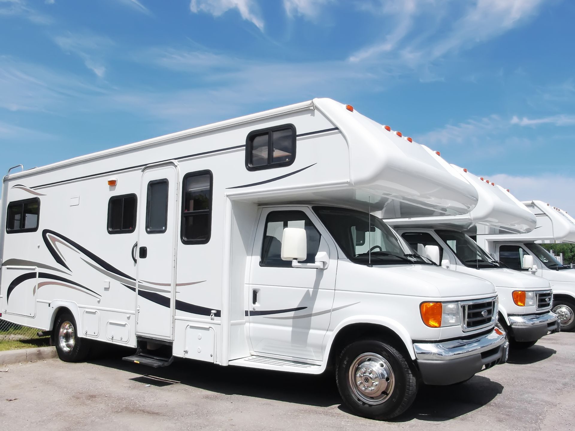 White RV camper van parked outdoors under a blue sky, with two similar RVs behind it