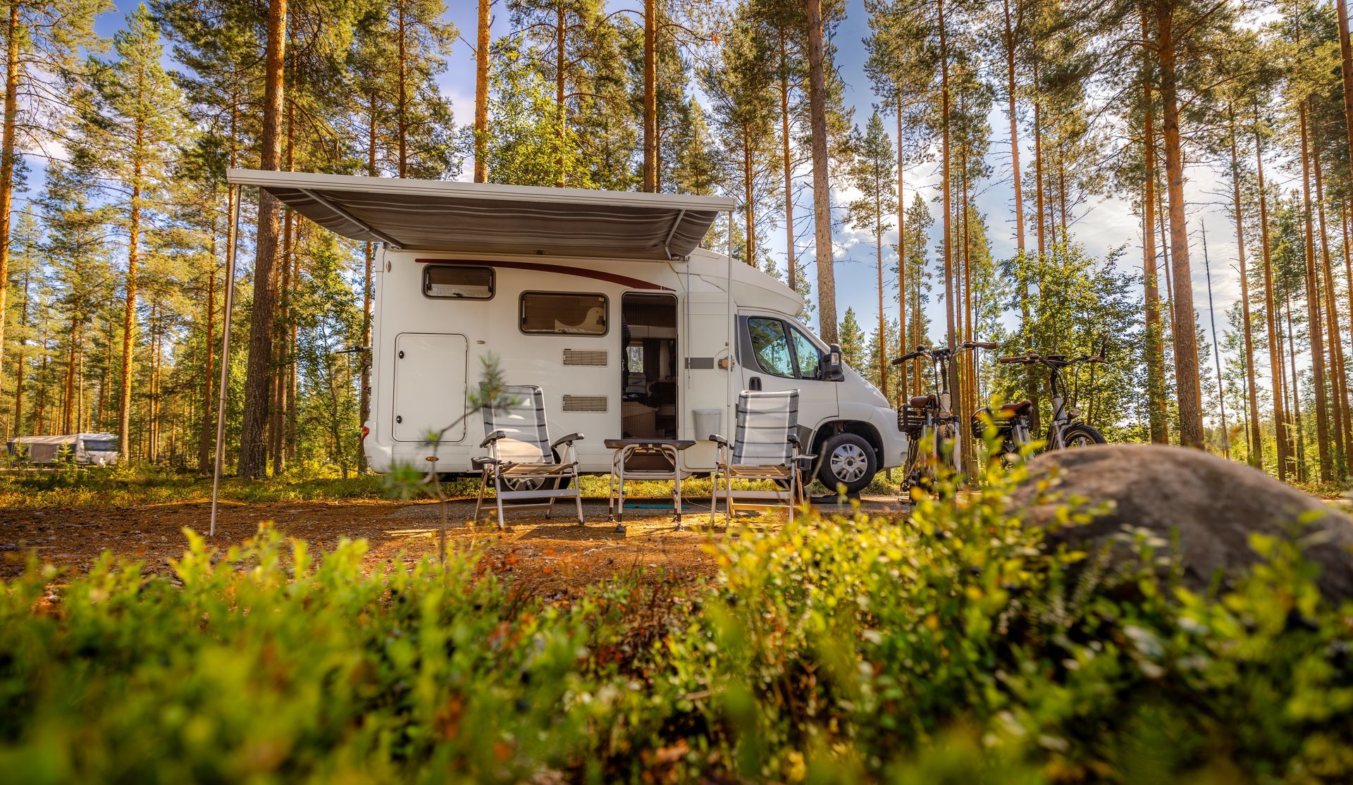 Camper van parked in a sunlit forest clearing beside a small white cabin