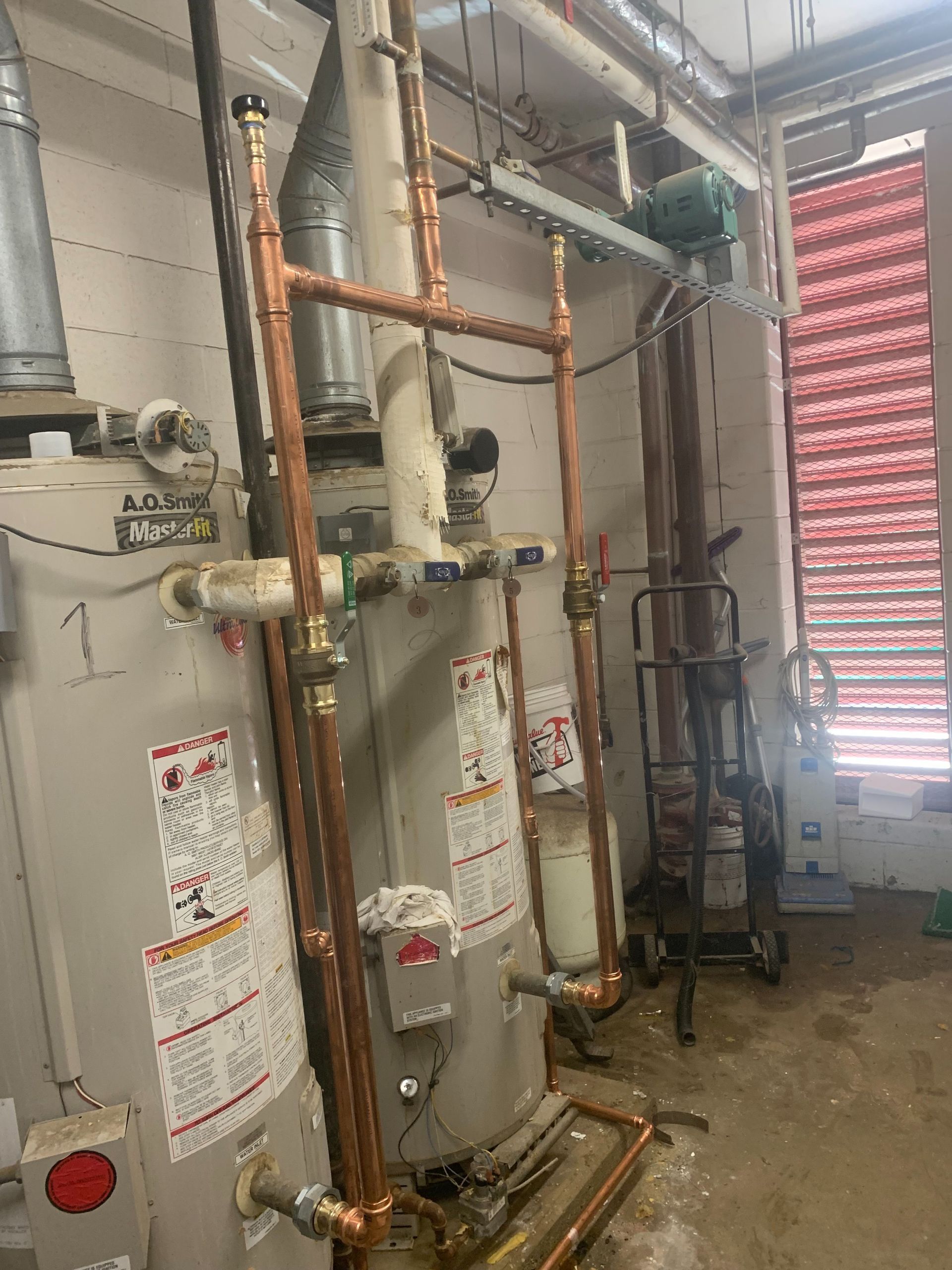 Two water heaters with copper piping in a utility room.
