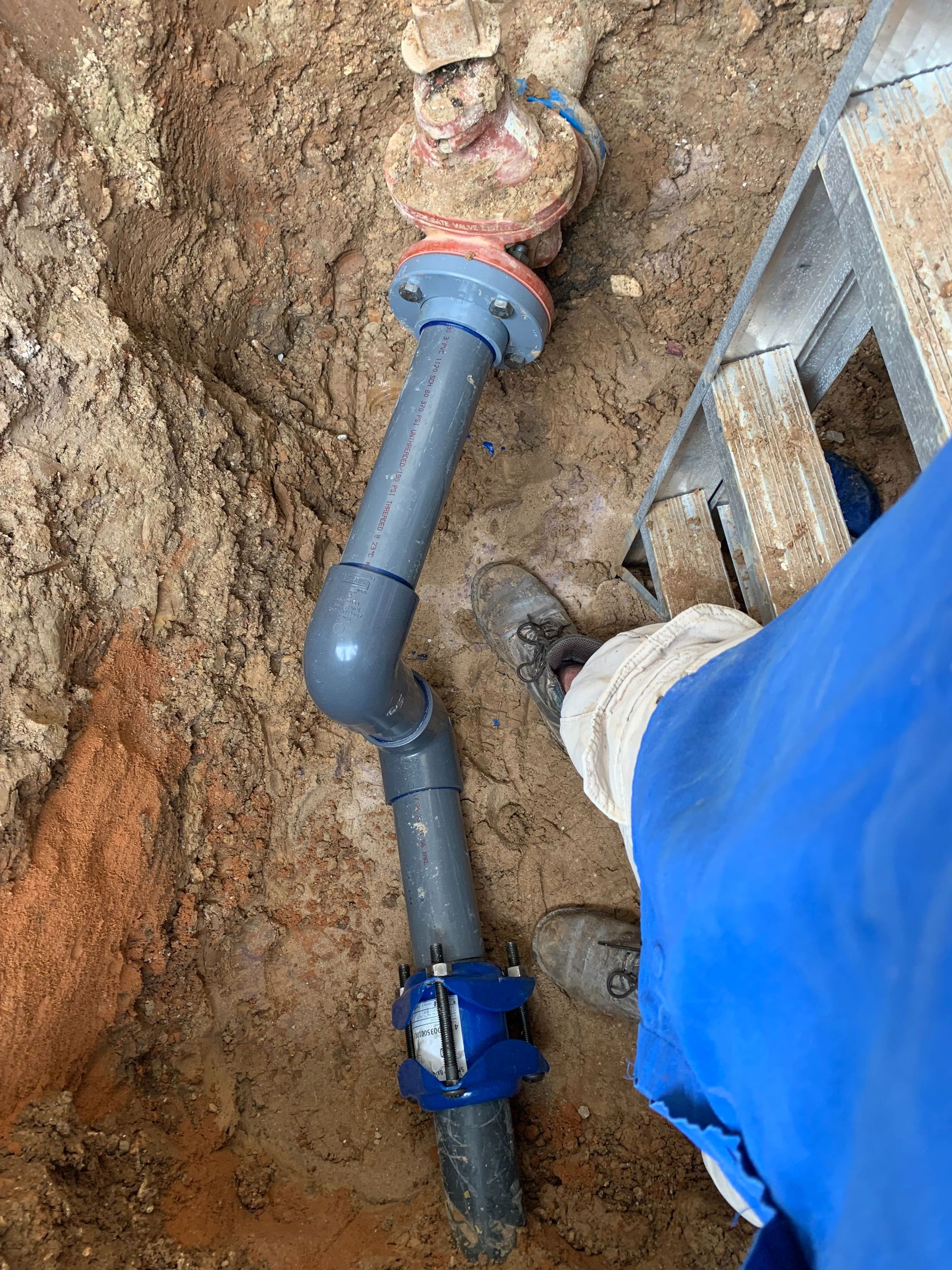 PVC pipes connected in an excavated ditch. A person in blue overalls and white gloves is working.