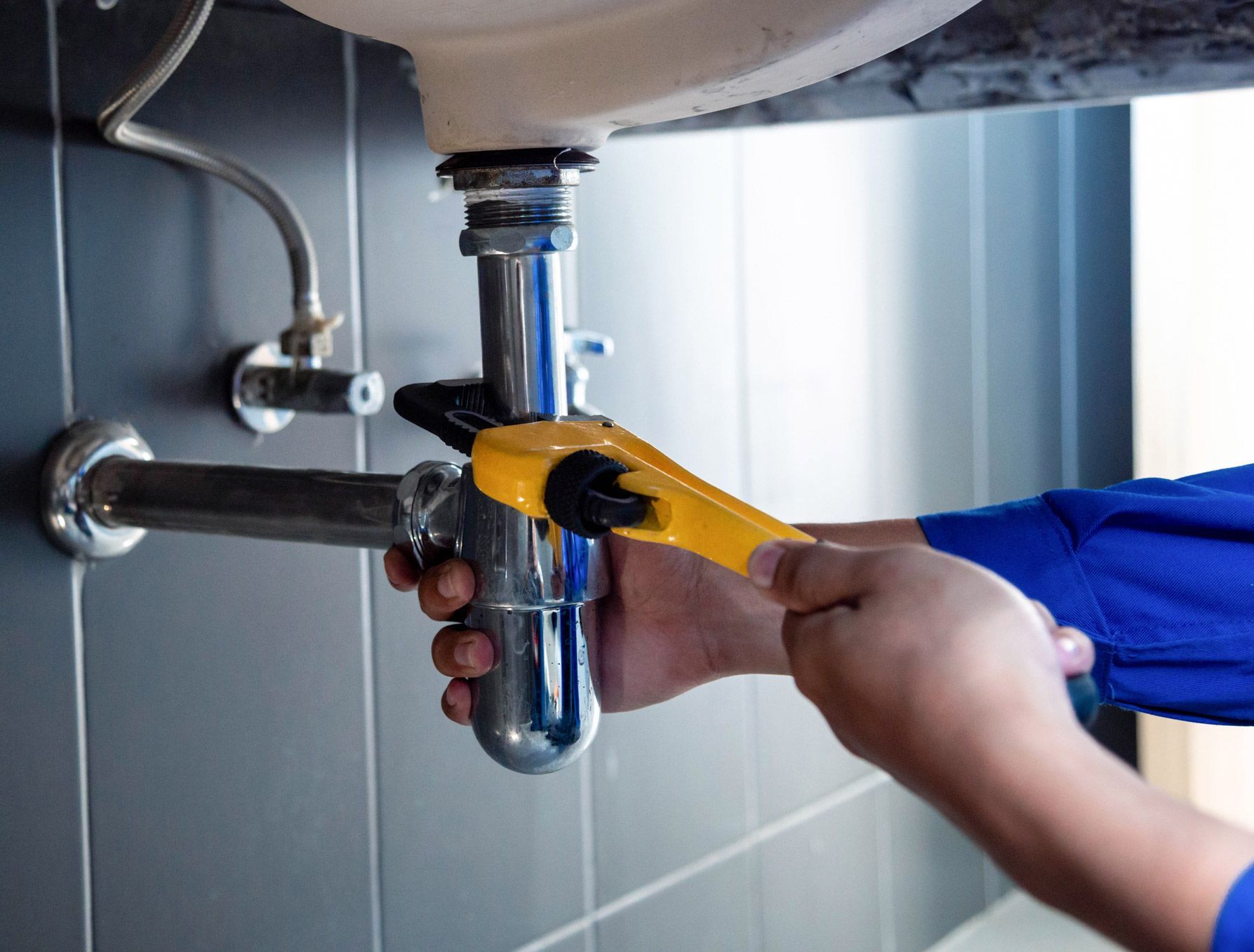 A plumber is fixing a sink pipe with a wrench.