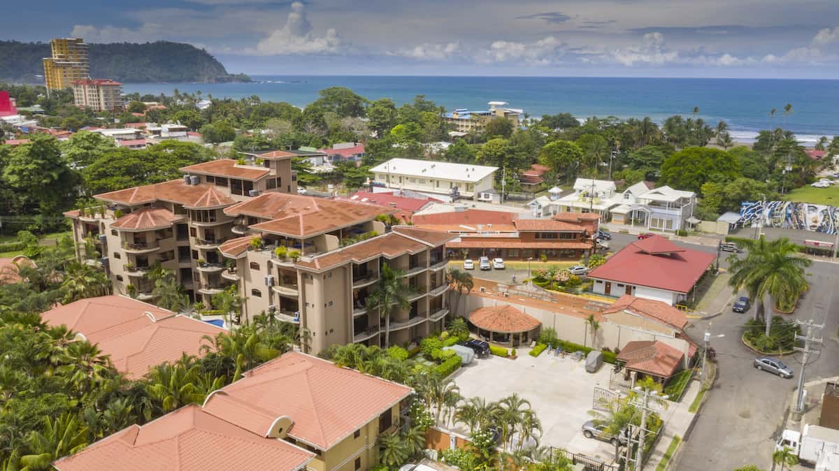 An aerial view of a city with a lot of buildings and trees near the ocean.
