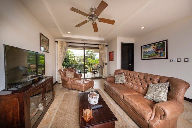A living room with a couch , chair , table , television and ceiling fan.
