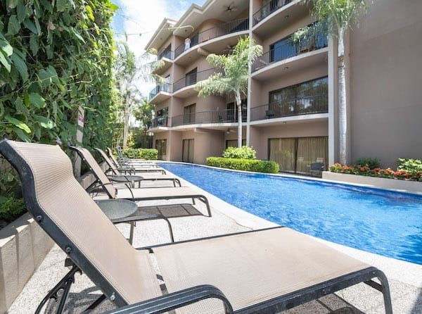 A row of lounge chairs sitting next to a swimming pool in front of a building.