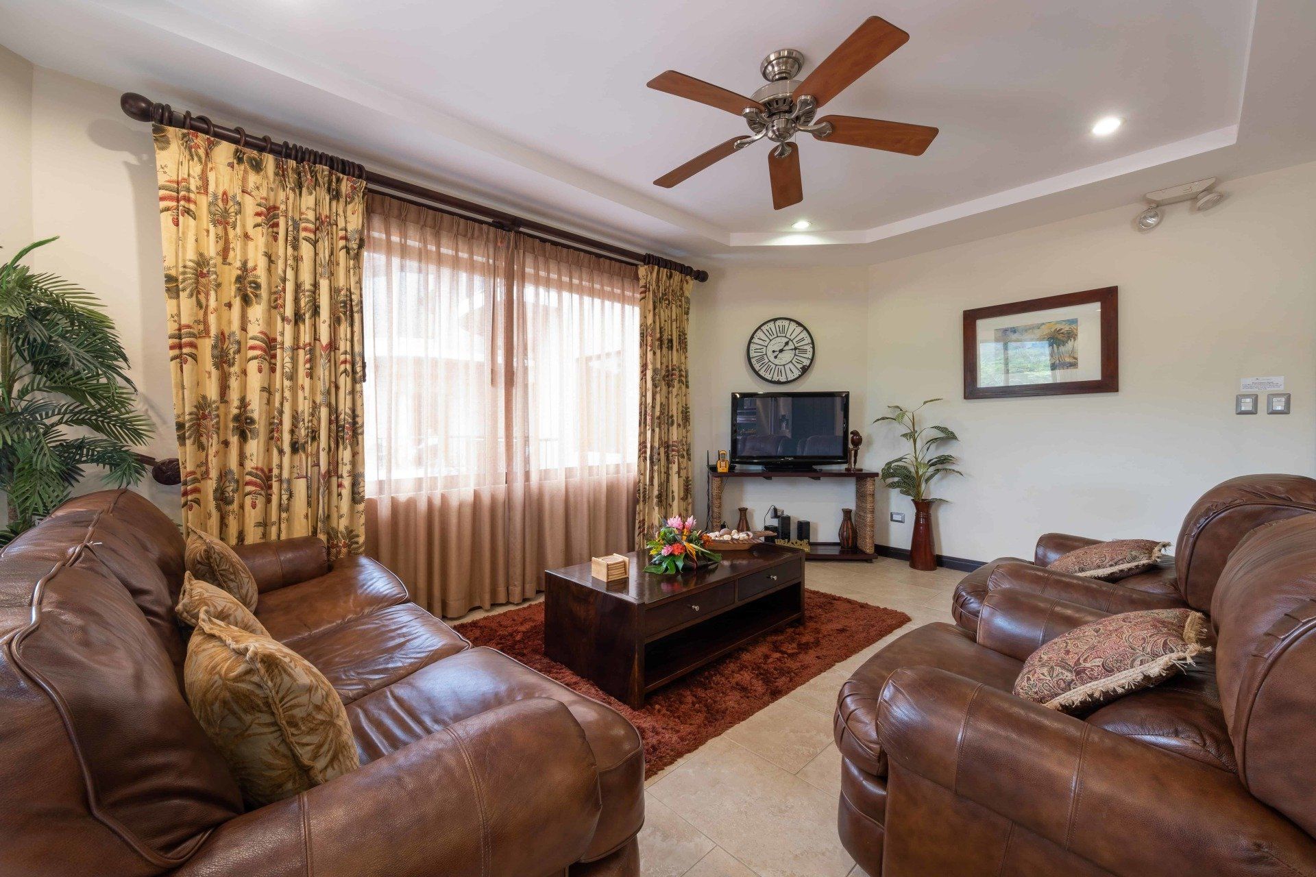 A living room with brown furniture and a ceiling fan