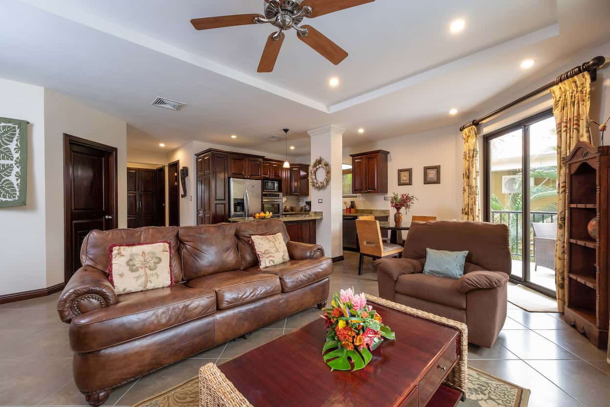 A living room with a couch , chair , coffee table and ceiling fan.