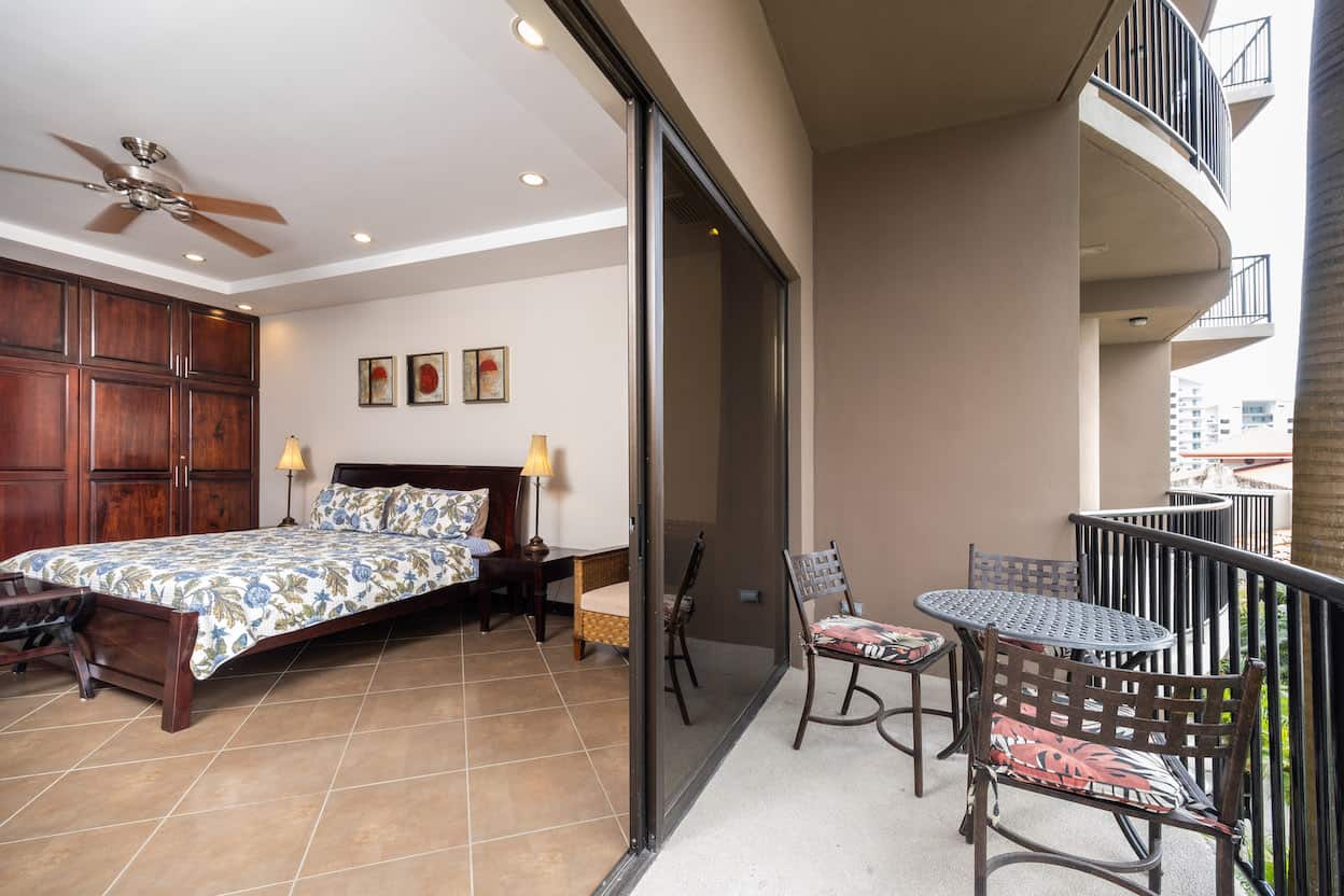 A bedroom with a large bed and a balcony with chairs and tables.