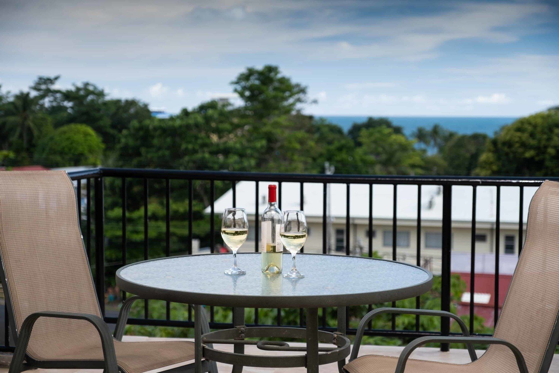 A table with two glasses of wine on it on a balcony overlooking the ocean.