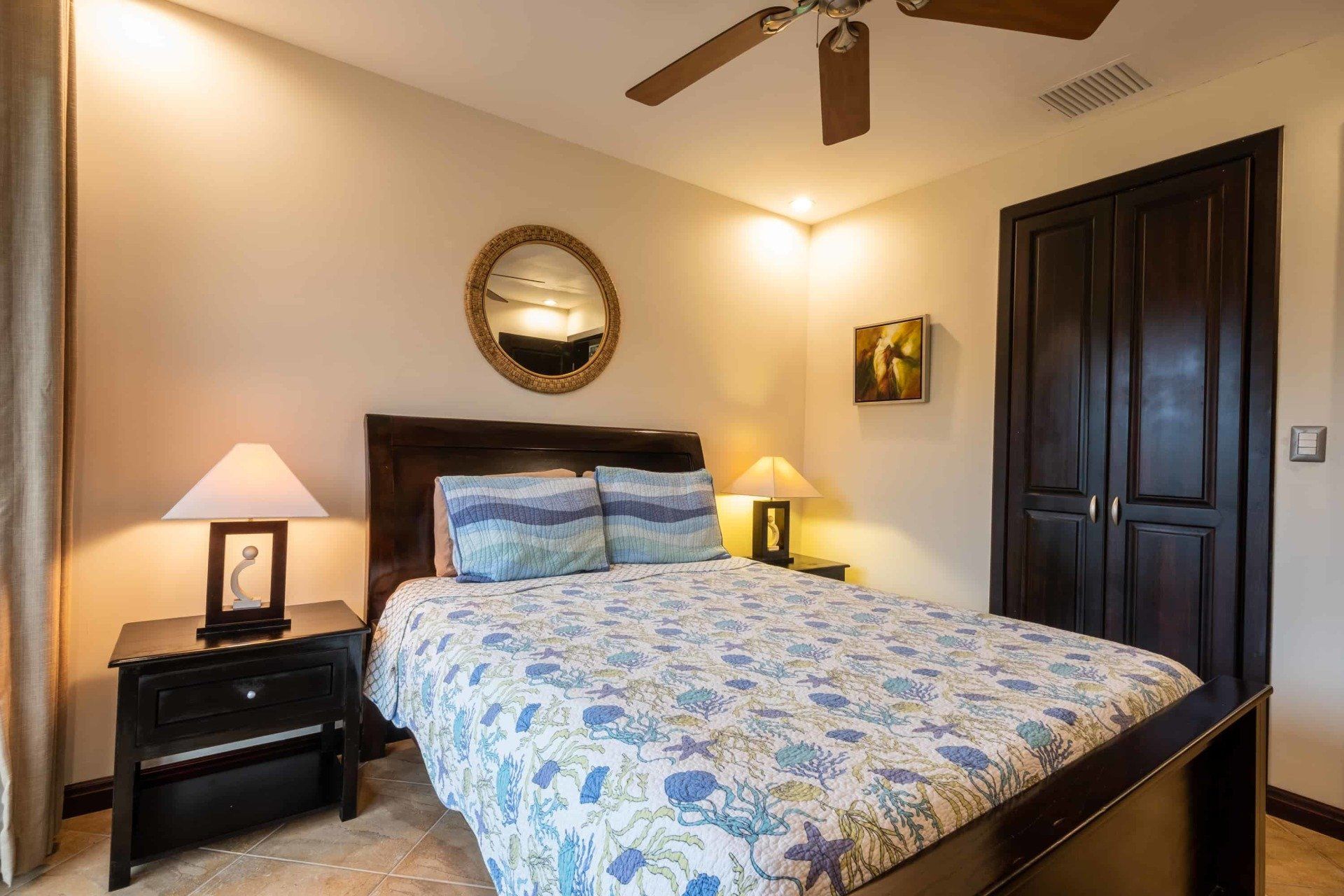 A bedroom with a bed , nightstand , lamps and a ceiling fan.