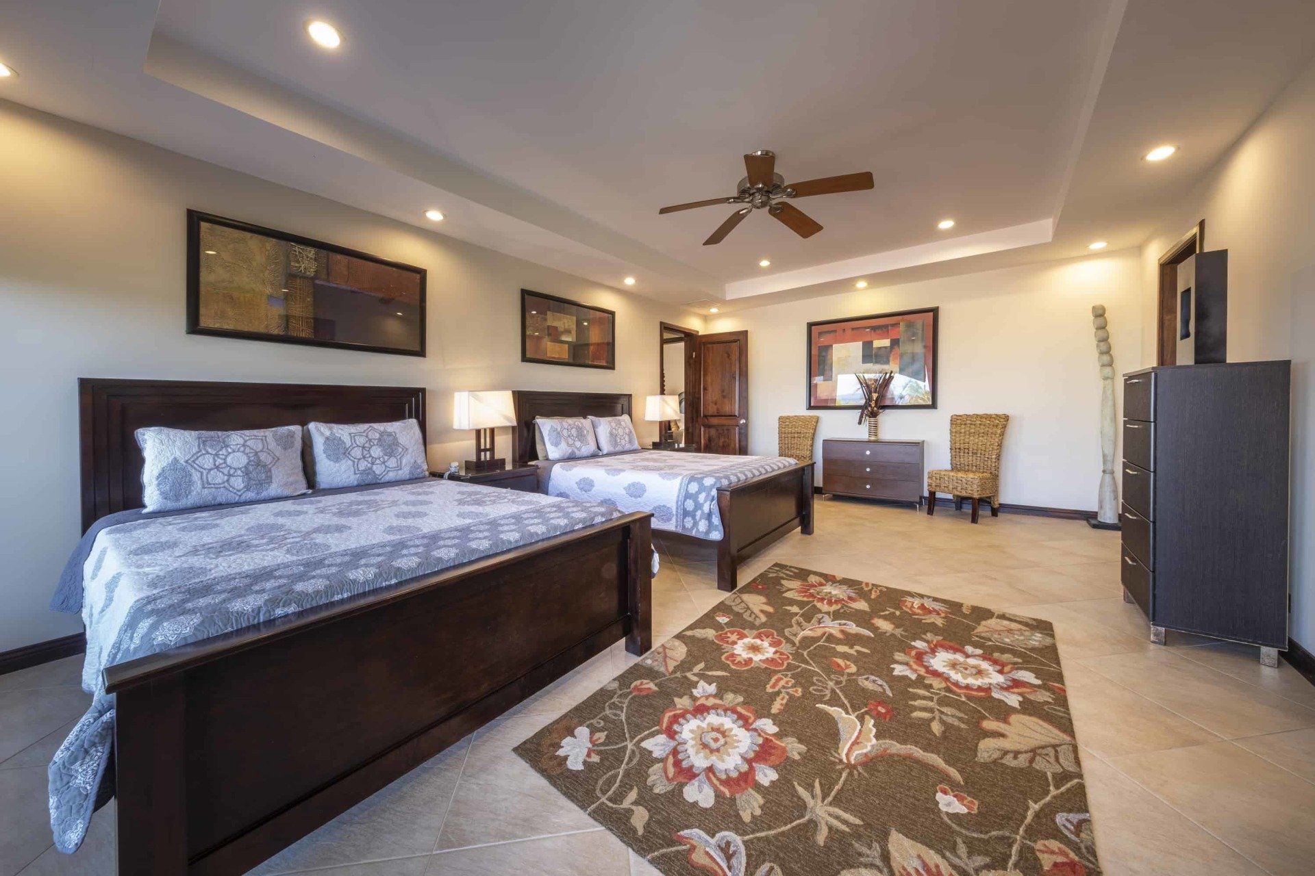 A bedroom with two beds , a rug , a dresser and a ceiling fan.