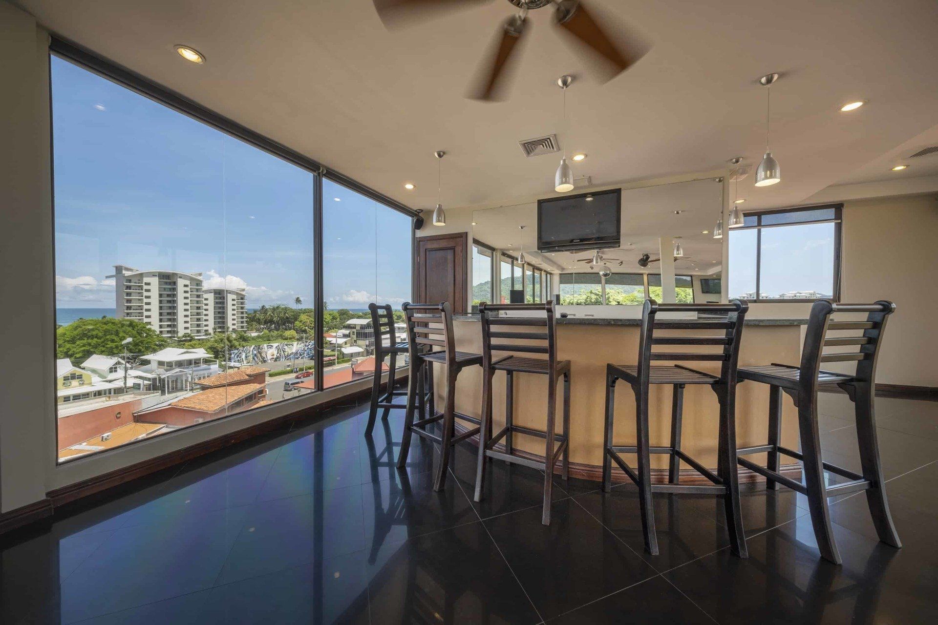 A large room with a bar and stools and a view of the ocean.