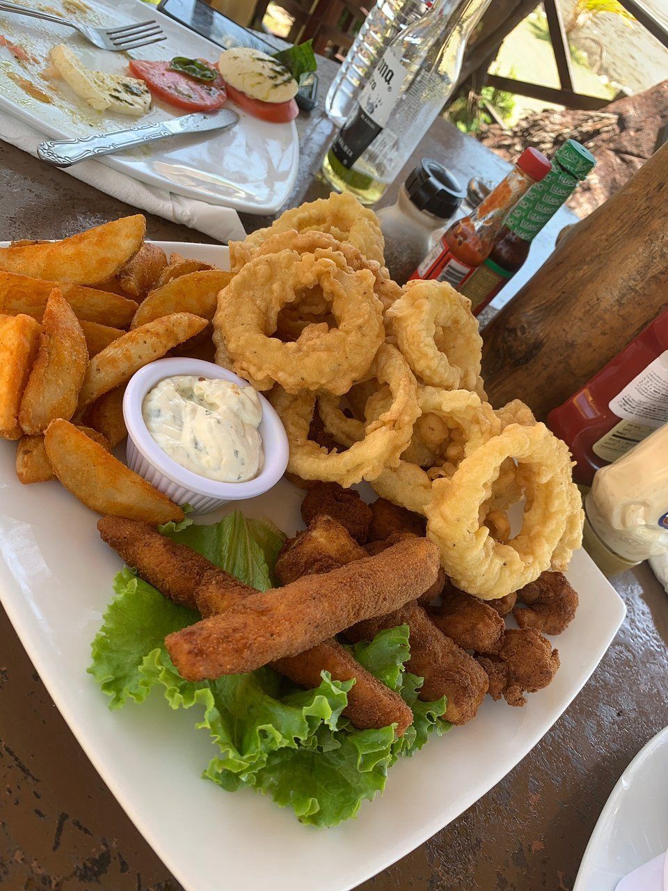 A plate of food with fries , onion rings , chicken fingers , and sauce on a table.