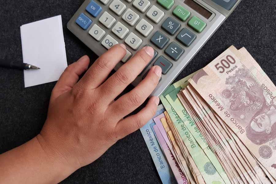 Una persona usa una calculadora junto a un montón de billetes de 500 pesos