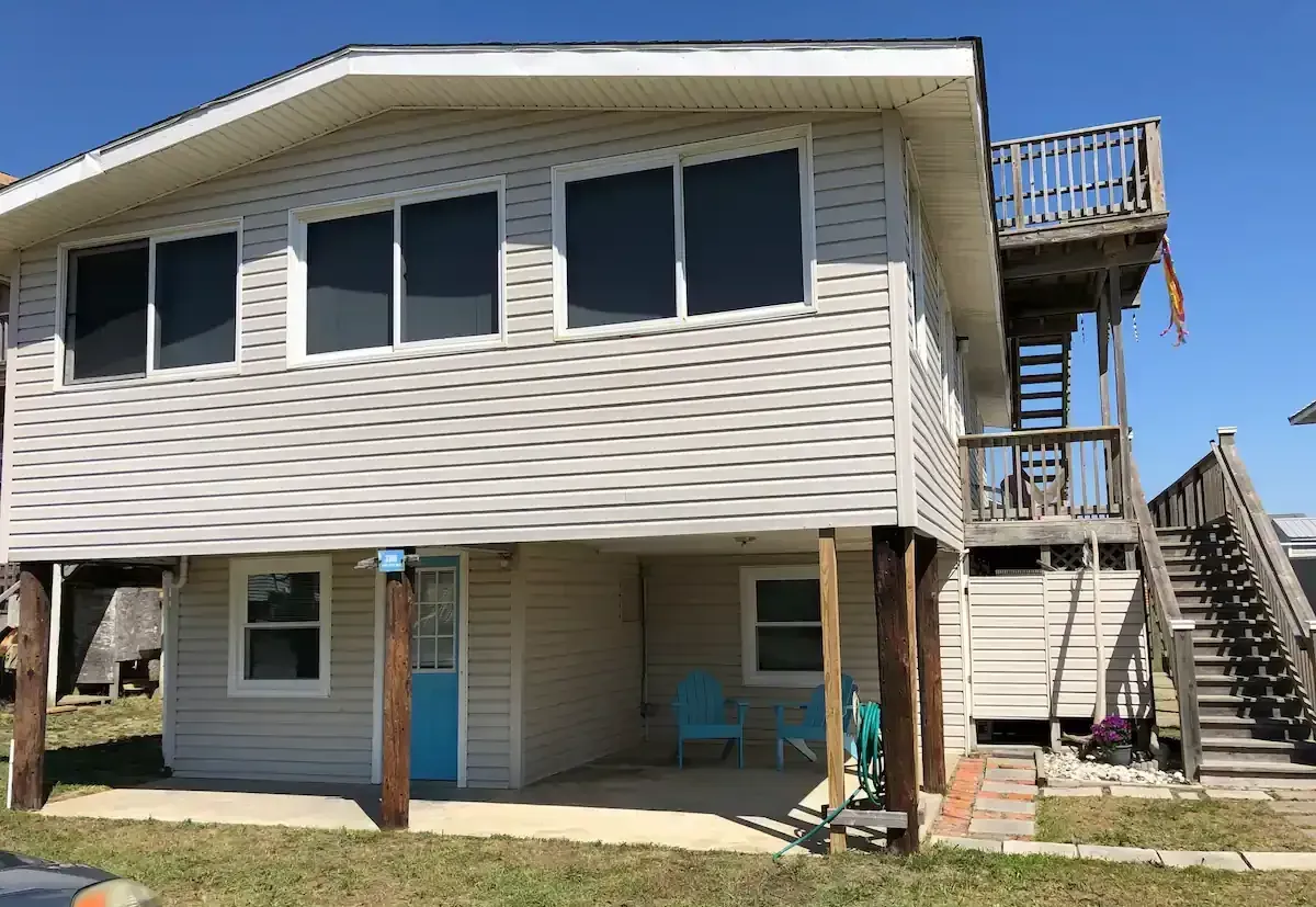 A white house with a blue door and stairs is sitting on top of a lush green field.