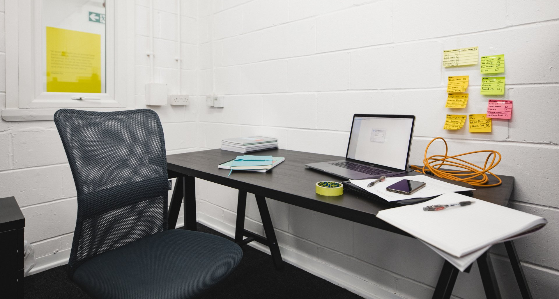 A desk with a laptop and sticky notes on the wall.