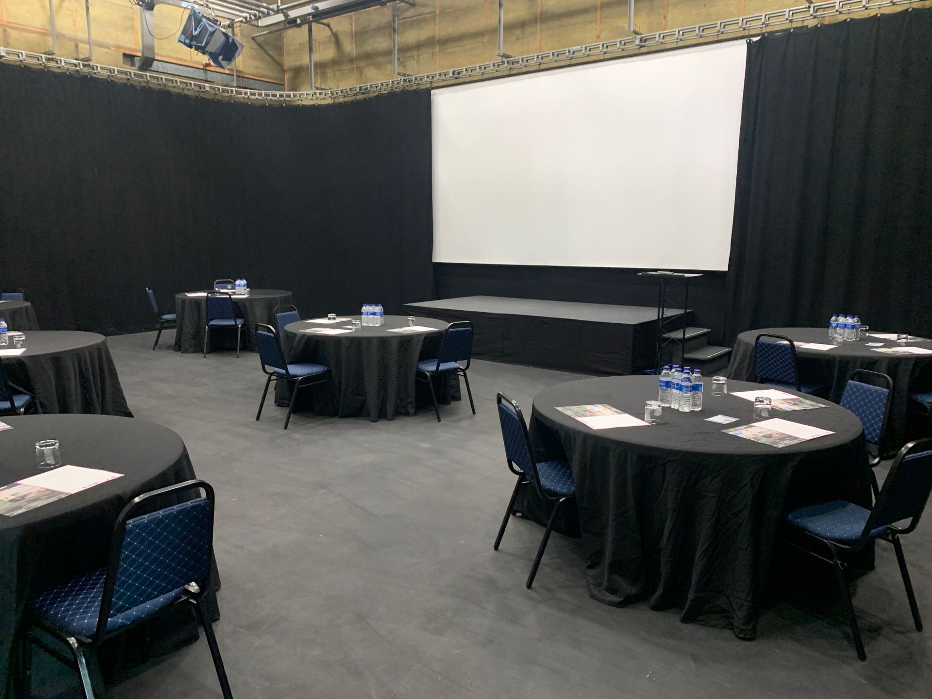 A room with tables and chairs and a large screen.