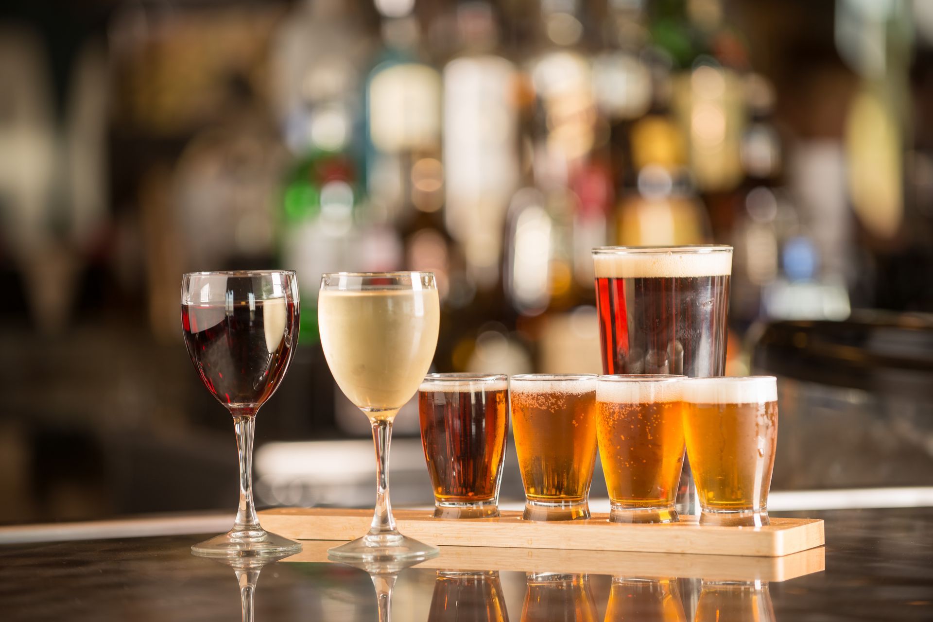 Assorted beer and wine glasses on a wooden tray in a bar with blurred bottles behind