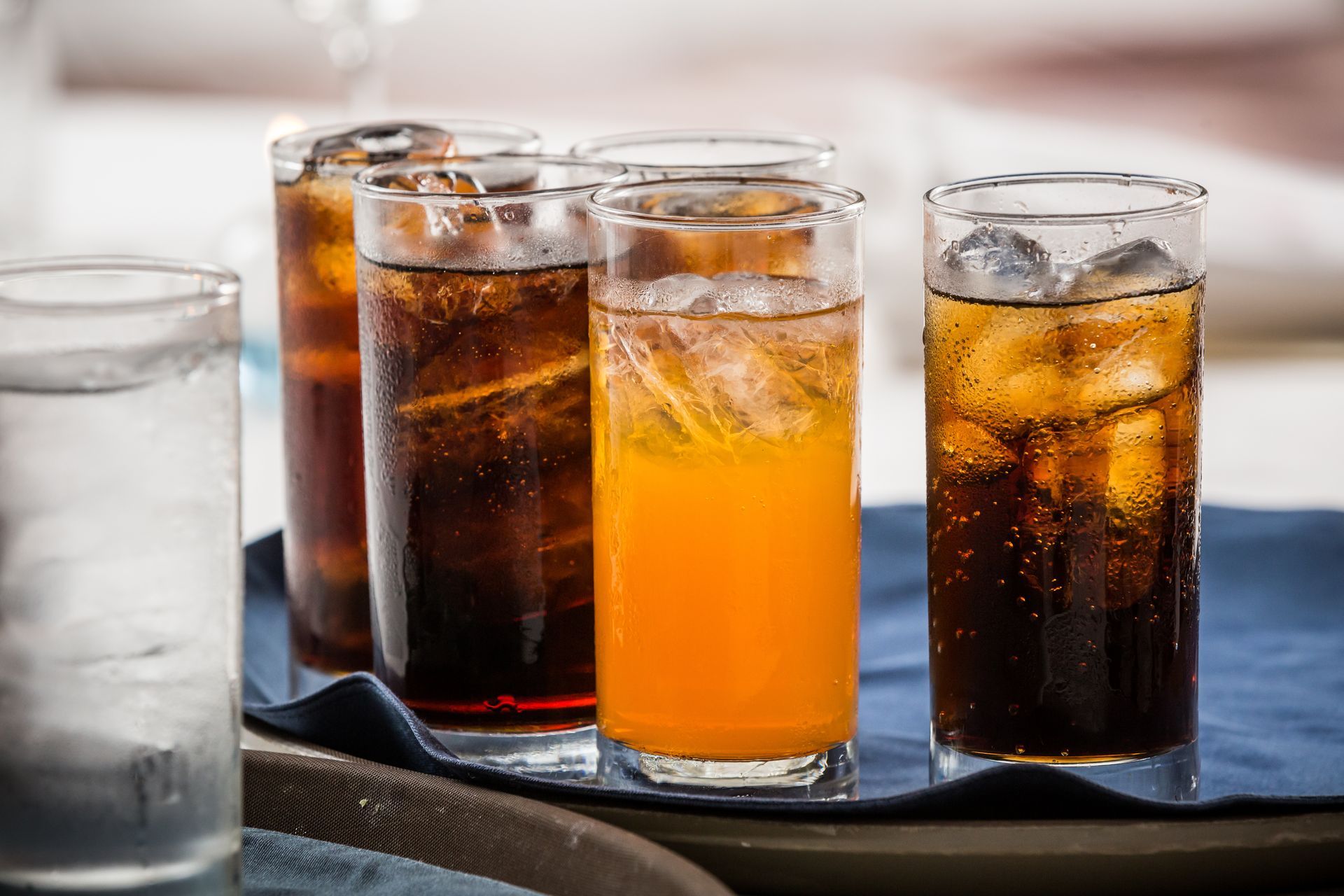 Four tall glasses of iced soda, including cola and orange drink, on a tray