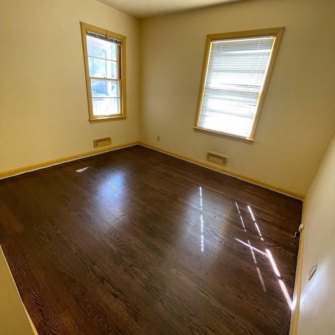 An empty room with hardwood floors and two windows.