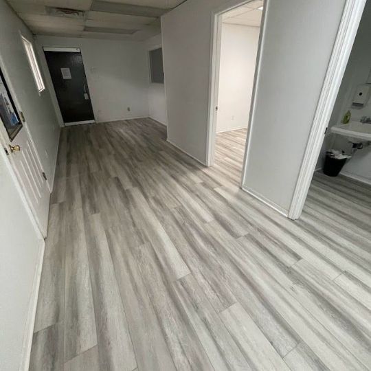 A hallway with hardwood floors and white walls leading to a bathroom.