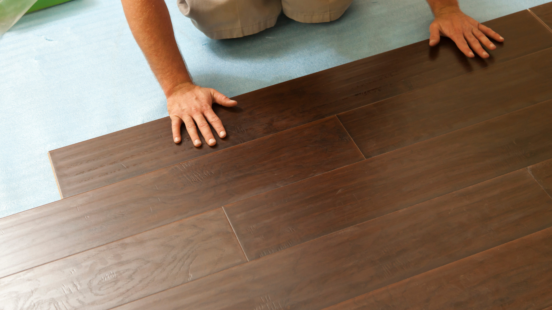 A person is installing a laminate floor with a wood design in a room.
