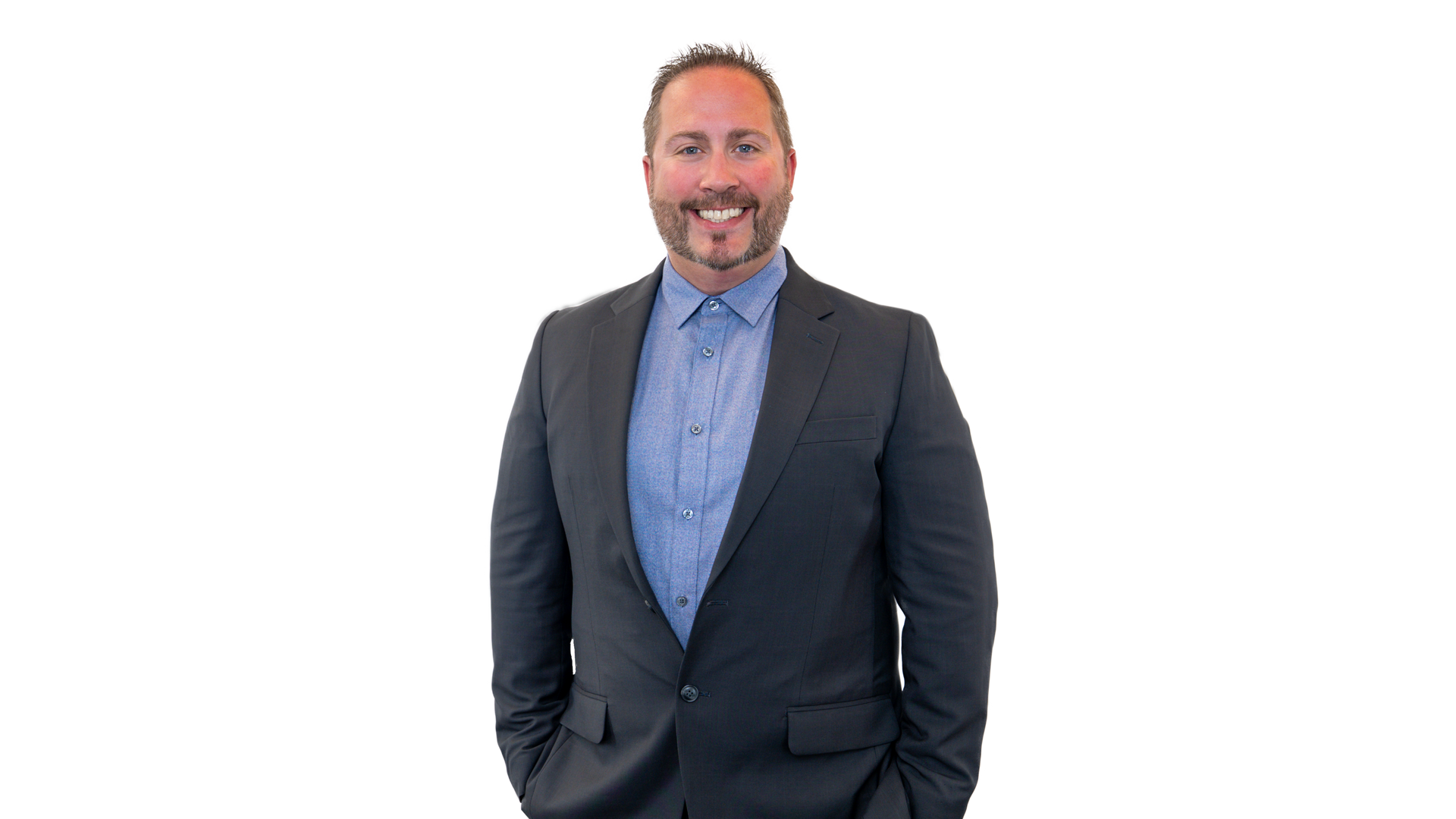 Man with a beard, wearing a blue suit and checkered shirt, smiling at the camera. White background.
