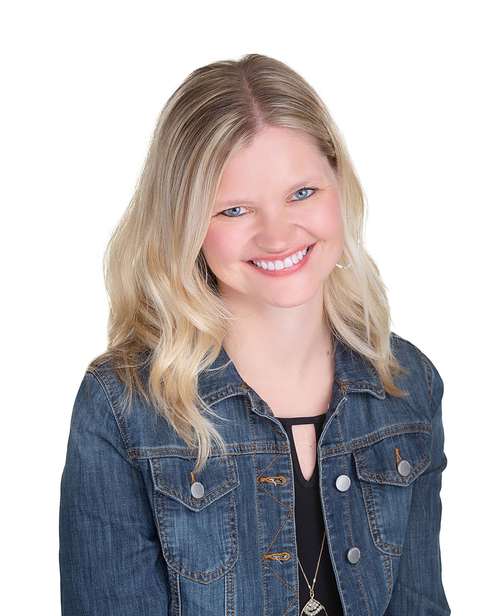 Blonde woman smiling, wearing a denim jacket over a black top, against a white background.