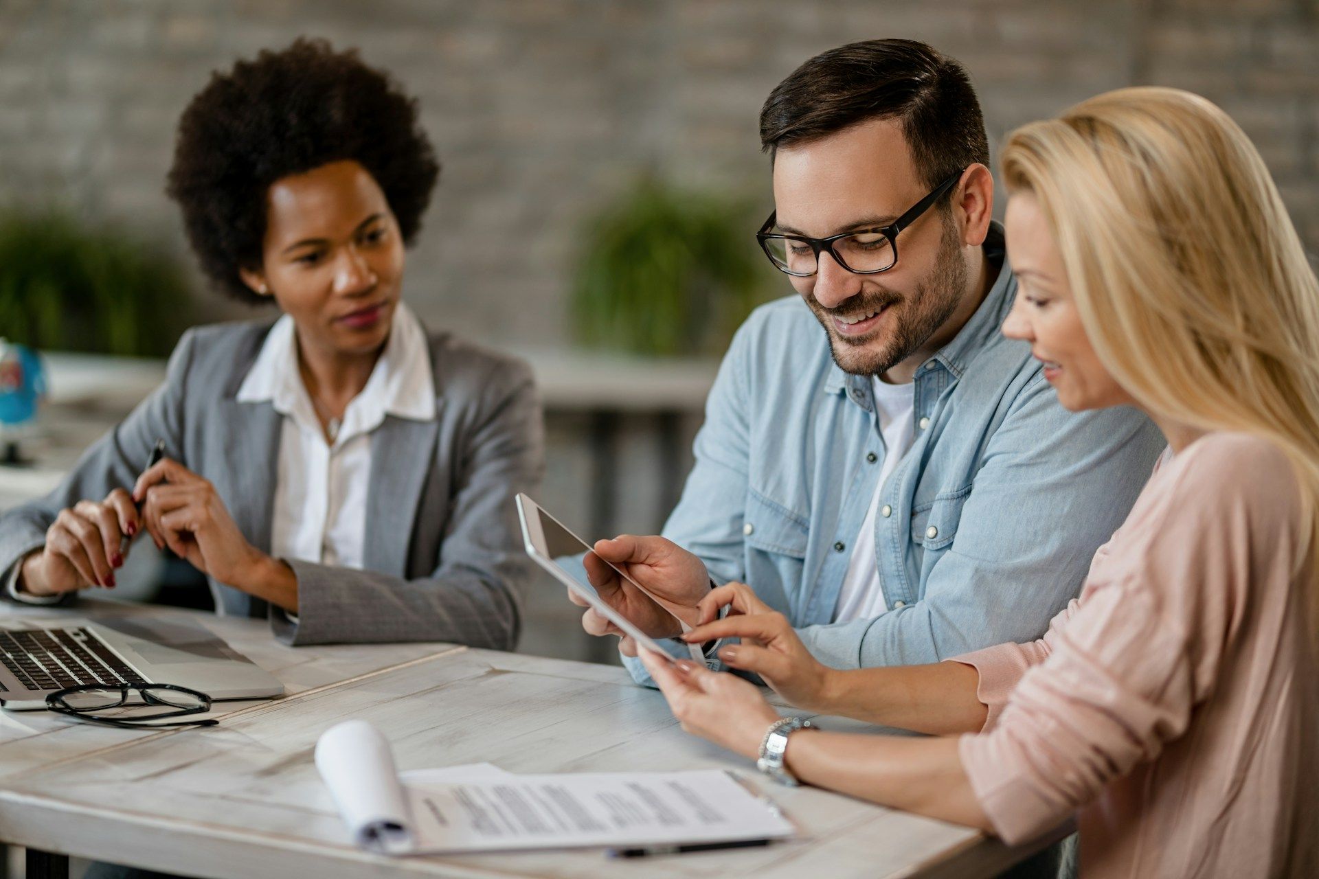 A financial advisor with a couple, reviewing documents and a tablet at a table.