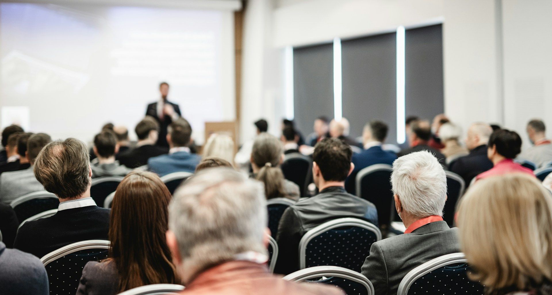A group of people are sitting in chairs in a conference room watching a presentation.