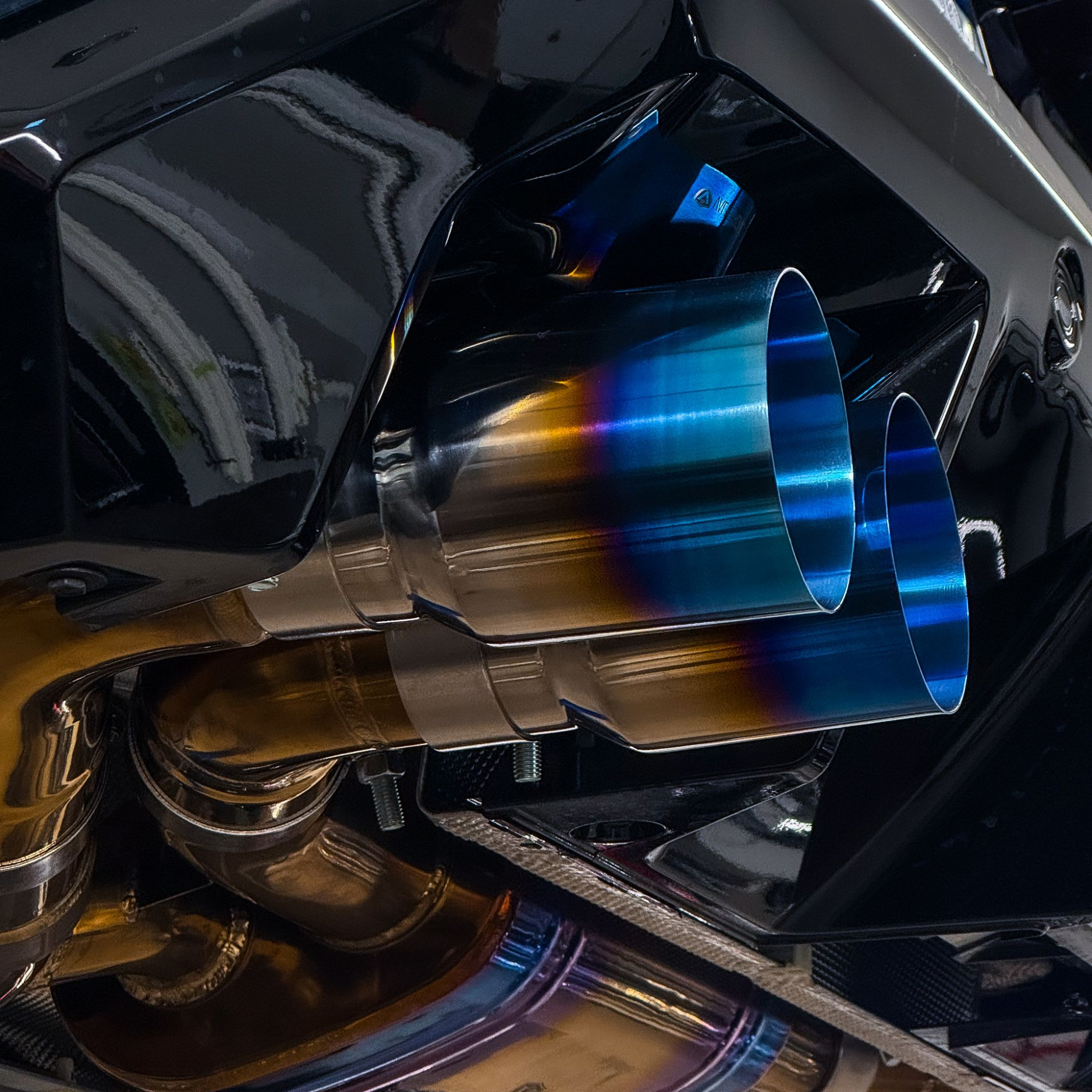 Close-up of a car's exhaust system, featuring blue and gold titanium exhaust tips.