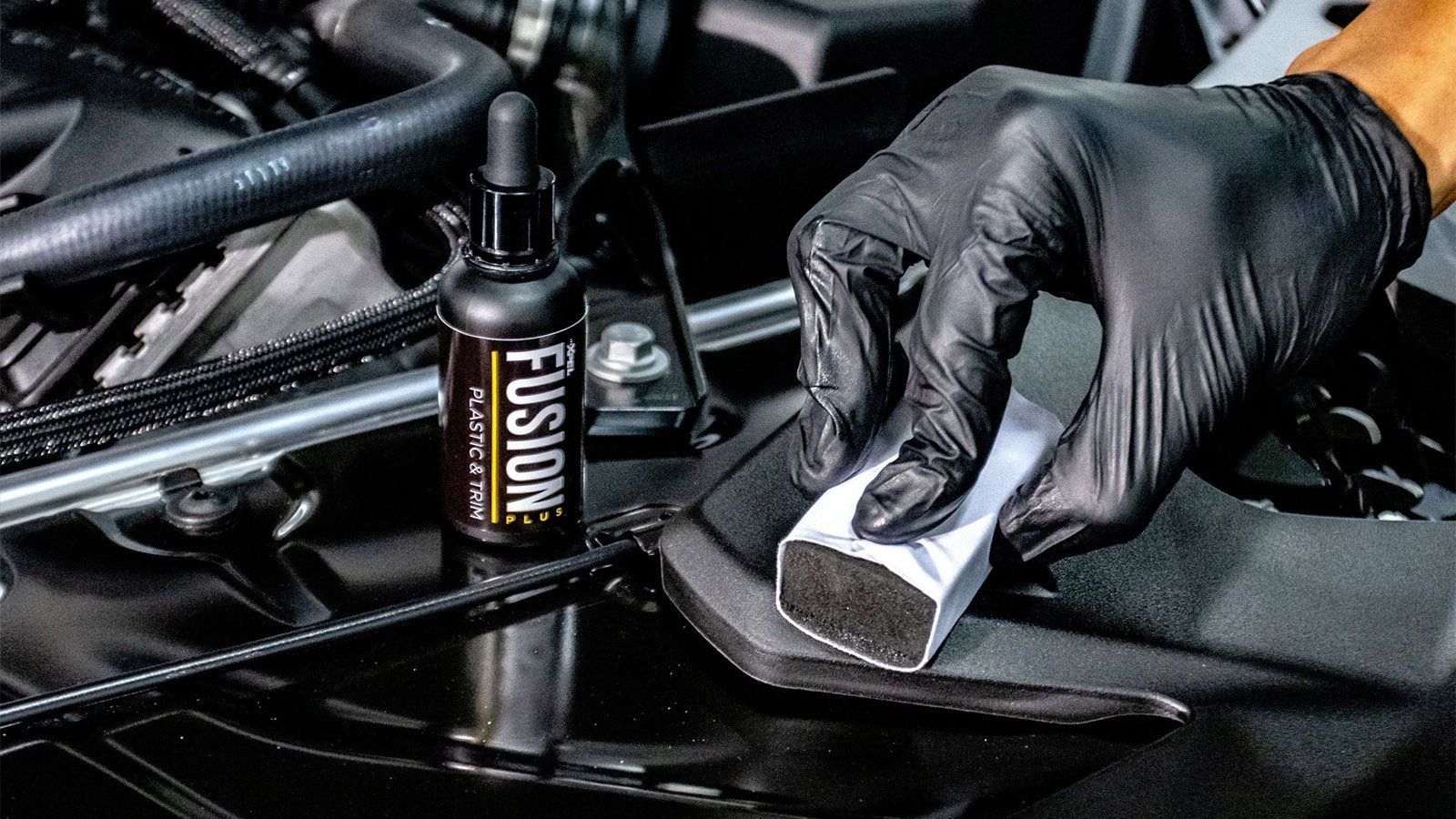 Gloved hand applying ceramic coating to car part with applicator. Bottle of