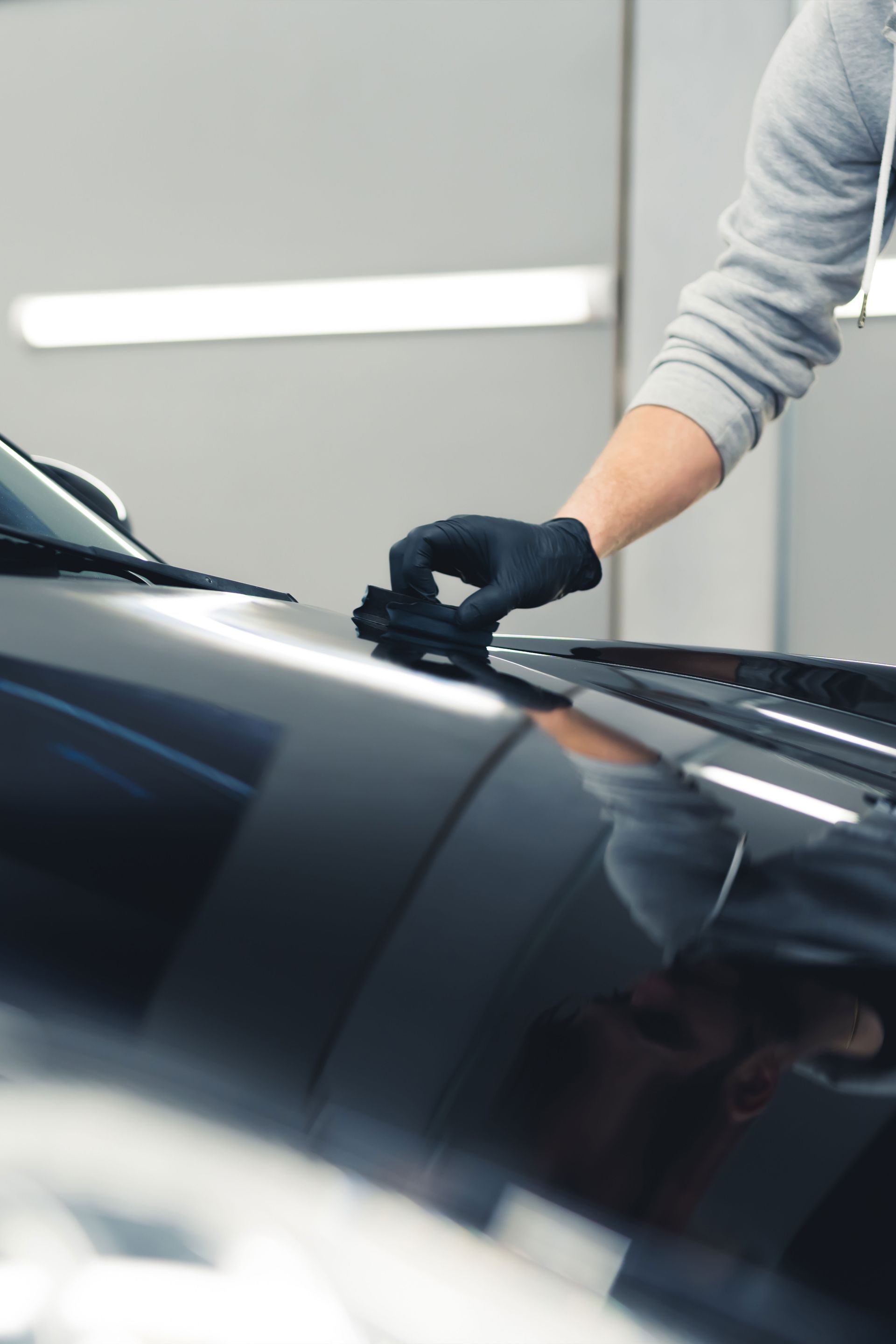 Person wearing black gloves applying product to the hood of a black car.