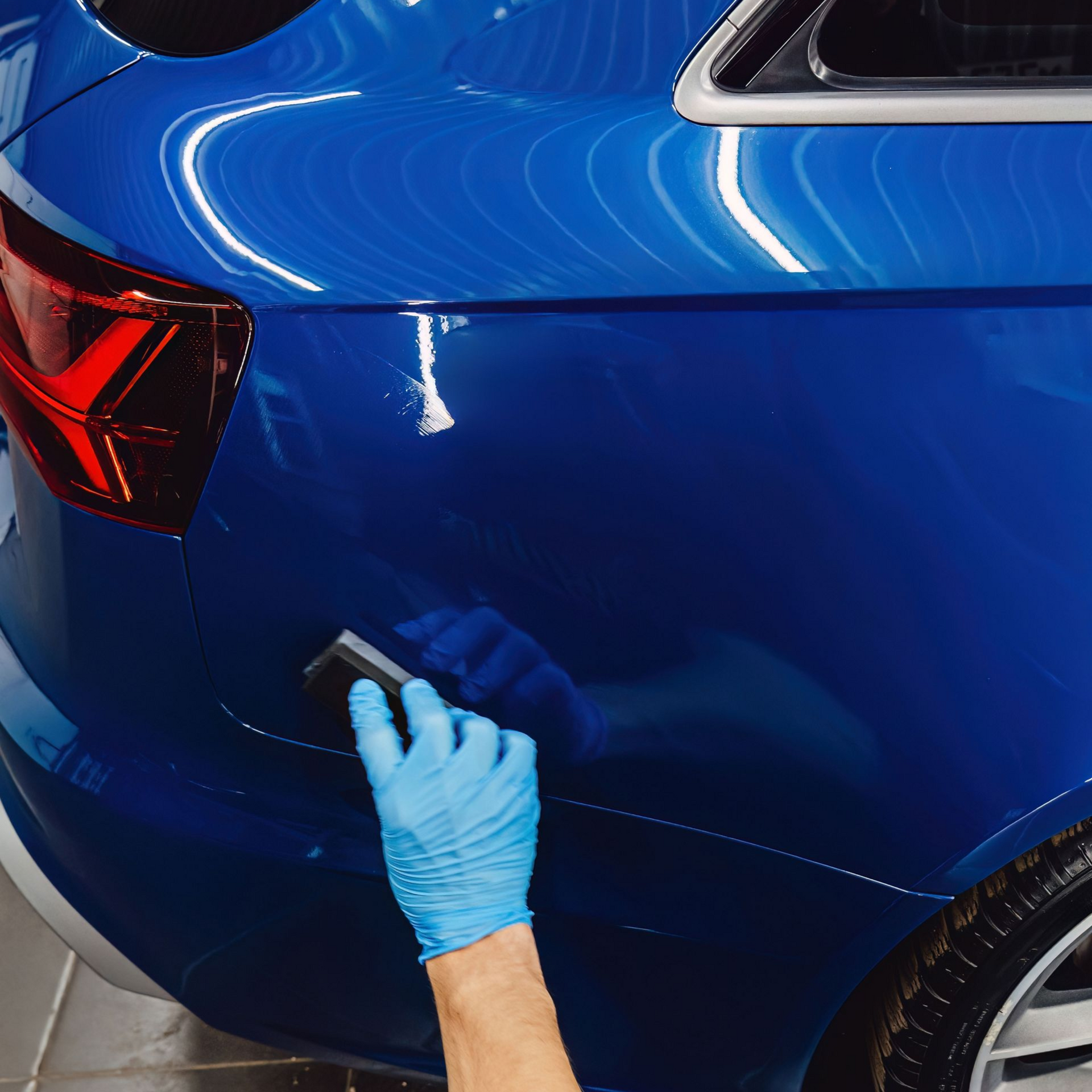 Hand in blue glove applying product to a blue car's shiny surface.