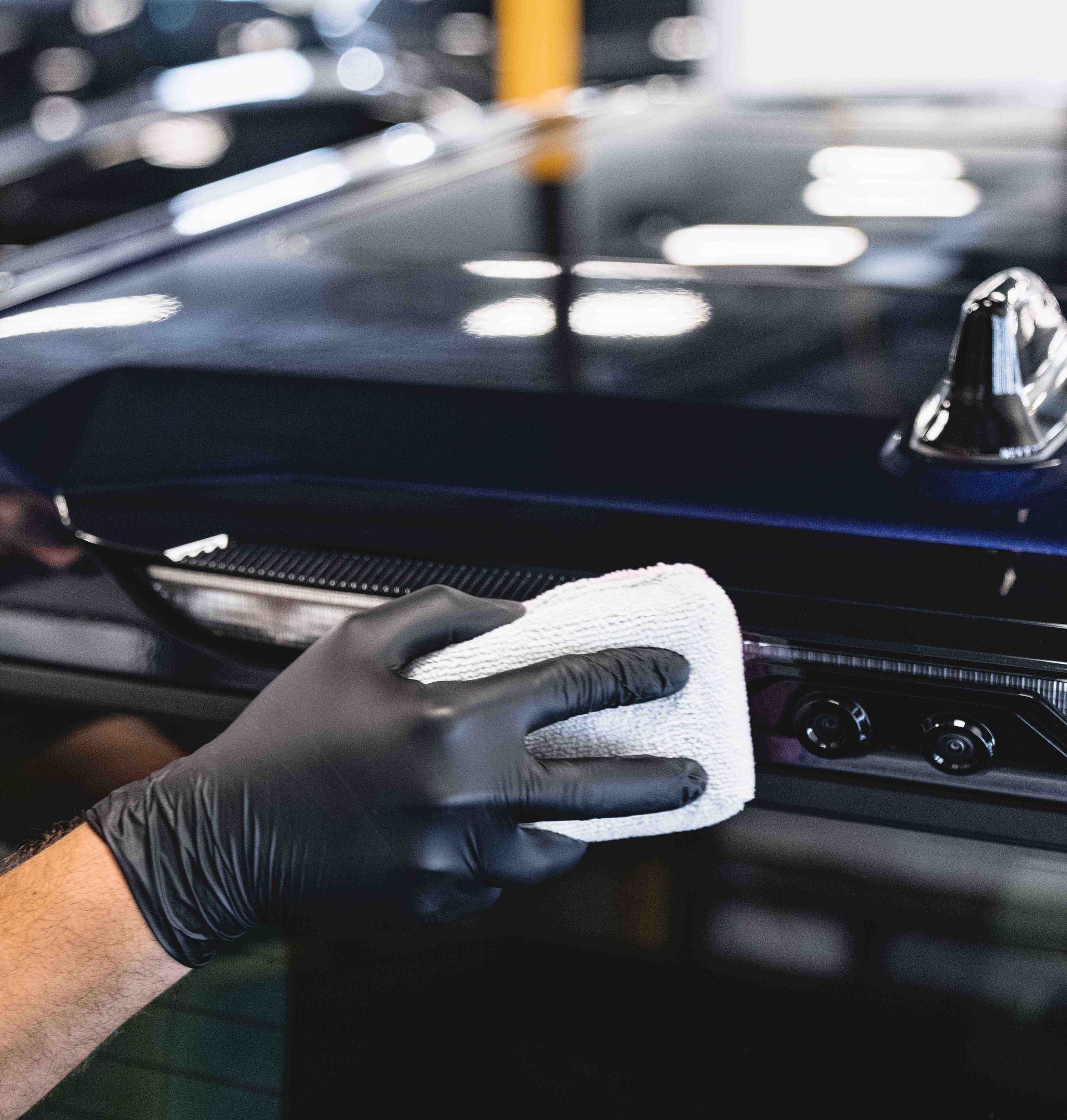 Gloved hand wiping a dark car with a white cloth, possibly detailing or cleaning.